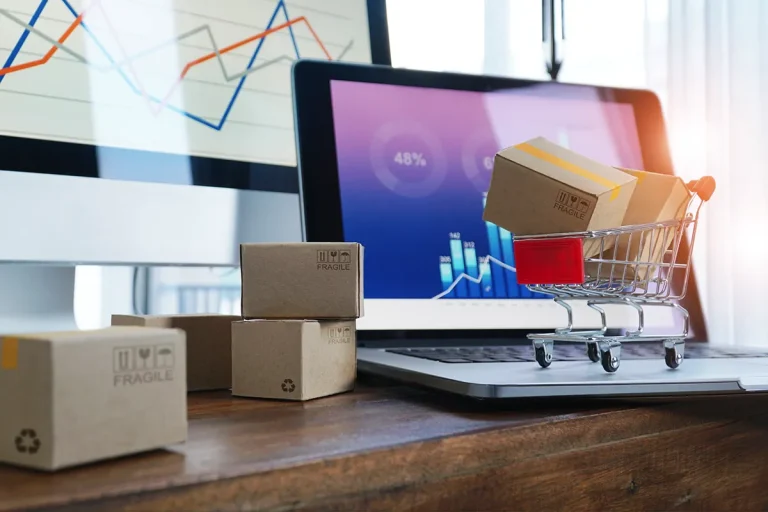Concept of online shopping, online retail, ecommerce. Boxes on table and in trolley on a laptop keyboard, and business graph growth on a screen background.